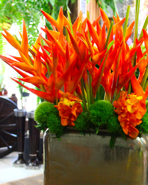 d’un vase en étain rectangulaire garni d’héliconias oranges et d’œillets green trick.